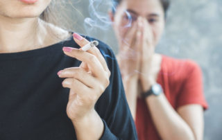 woman covering her face to protect from secondhand smoke drifting off a cigarette